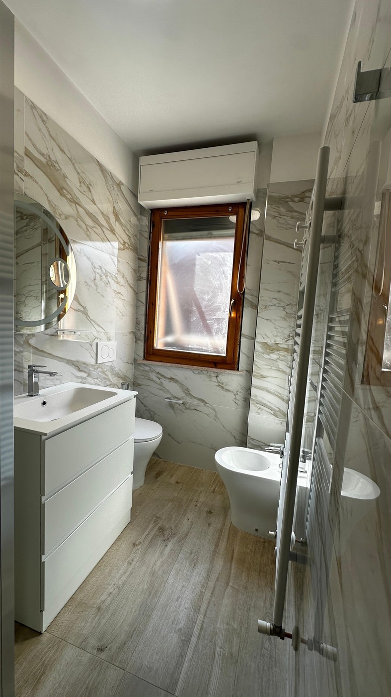 Panoramica completa bagno calacatta: sanitari sospesi, box doccia, scaldasalviette e pavimento legno — Senigallia 2026